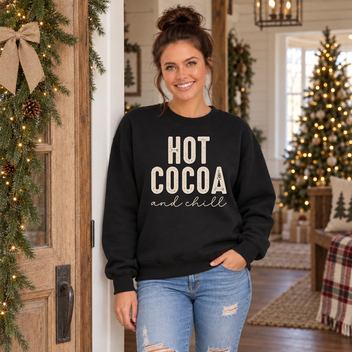 Woman wearing a black Hot Cocoa and Chill sweatshirt at a farmhouse doorway decorated for Christmas