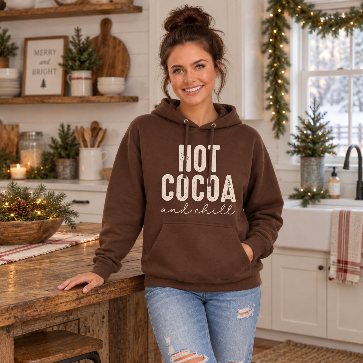 Woman wearing a brown Hot Cocoa and Chill hoodie in a Christmas farmhouse kitchen