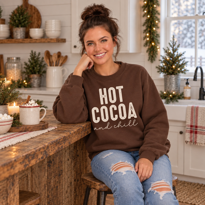 Woman wearing a brown sweatshirt with Hot Cocoa and Chill design beside a mug of cocoa in a cozy holiday kitchen