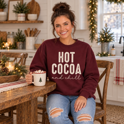 Woman wearing a maroon sweatshirt with Hot Cocoa and Chill design while holding a mug of cocoa in a holiday kitchen