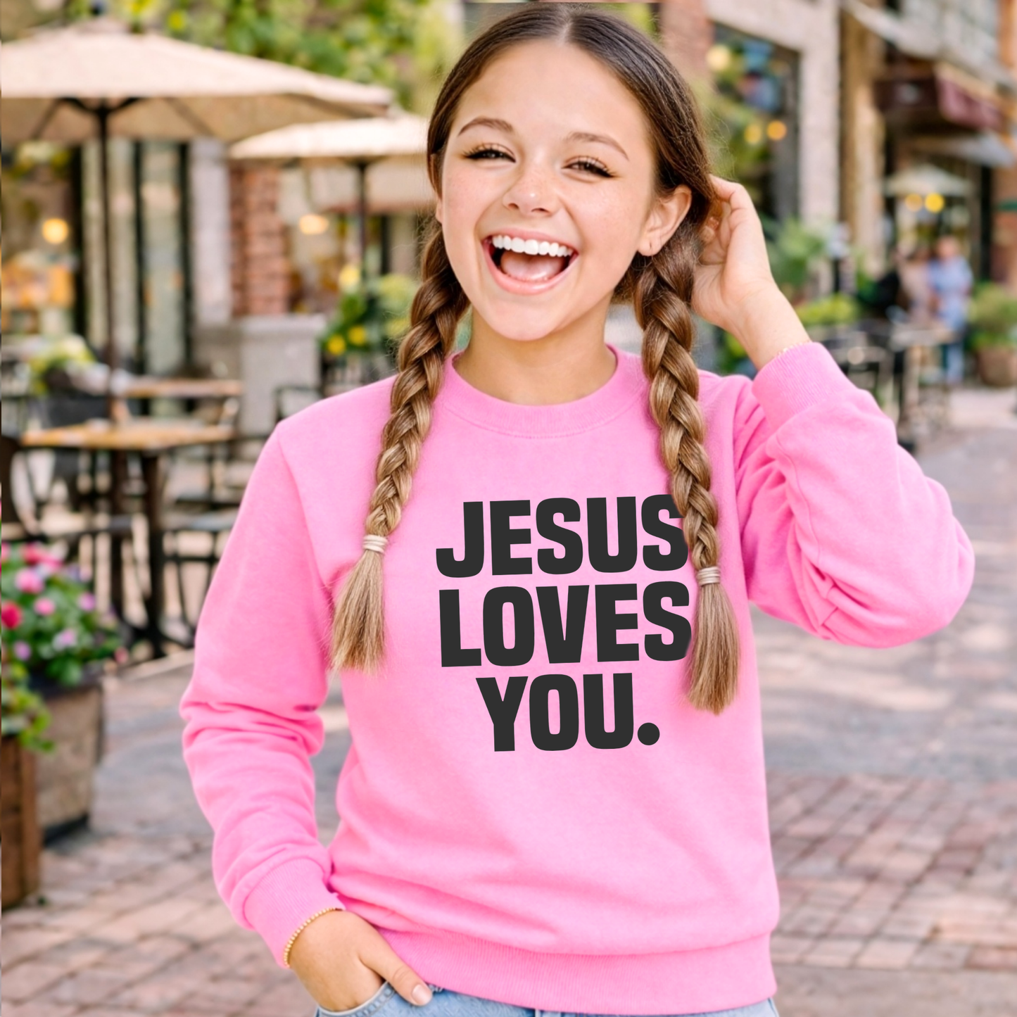 Child wearing a pink sweatshirt with 'Jesus Loves You' text, standing against a light background.