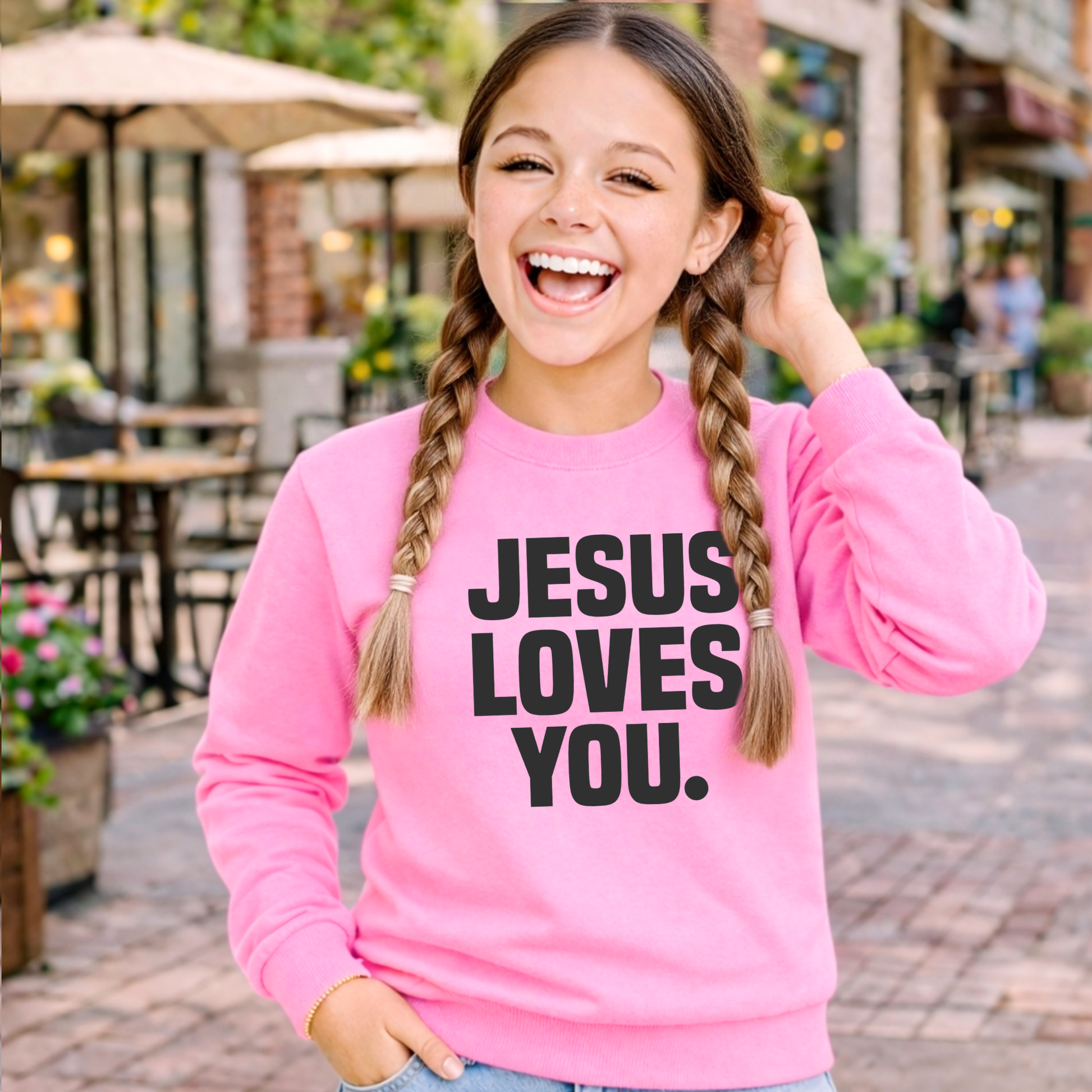 Child wearing a pink sweatshirt with 'Jesus Loves You' text, standing against a light background.