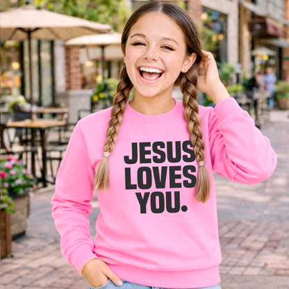 Child wearing a pink sweatshirt with 'Jesus Loves You' text, standing against a light background.