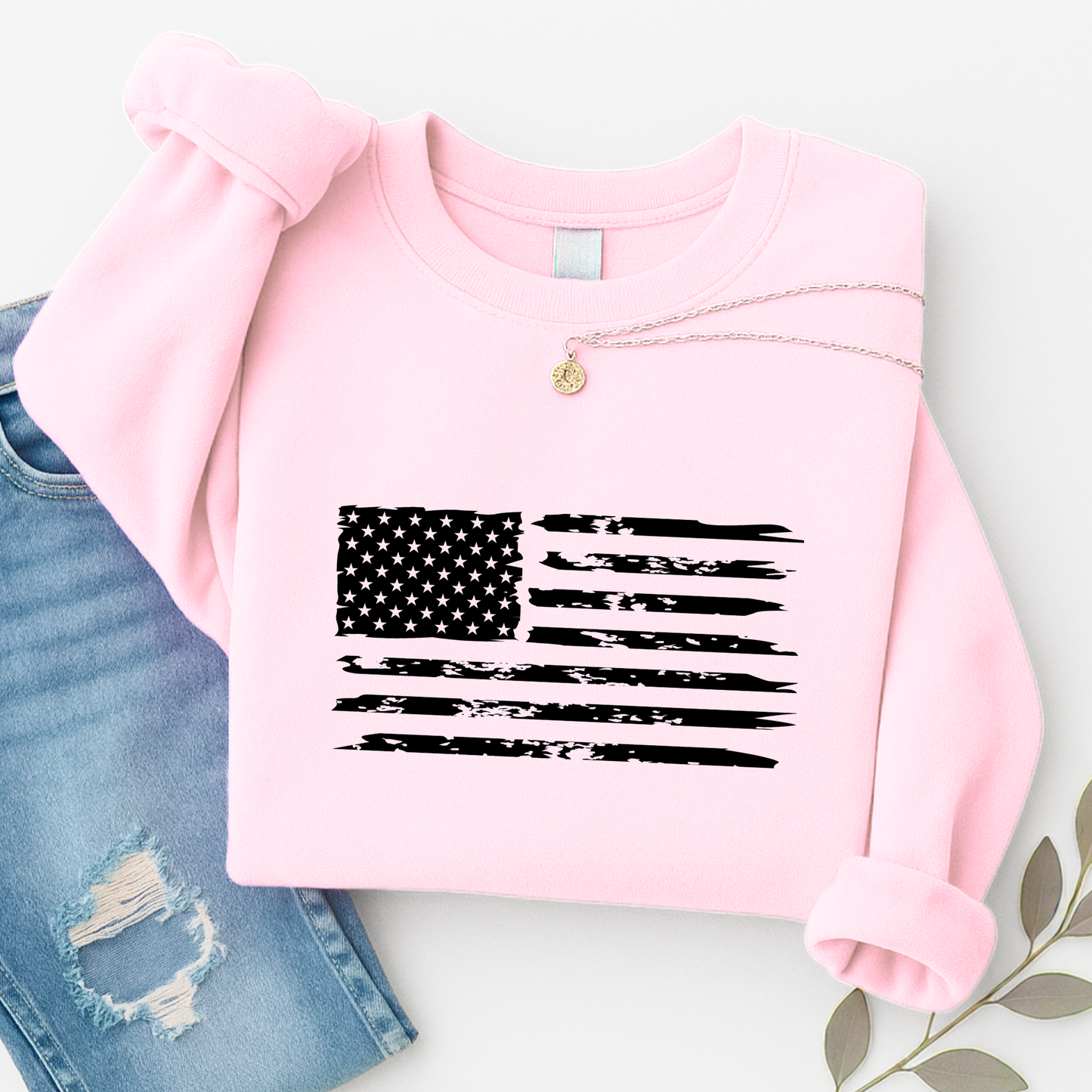 Pink sweatshirt with American flag design on a white surface with denim jeans.