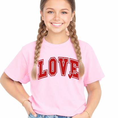 Youth girl wearing a light pink LOVE graphic t-shirt with red varsity lettering and light wash denim shorts