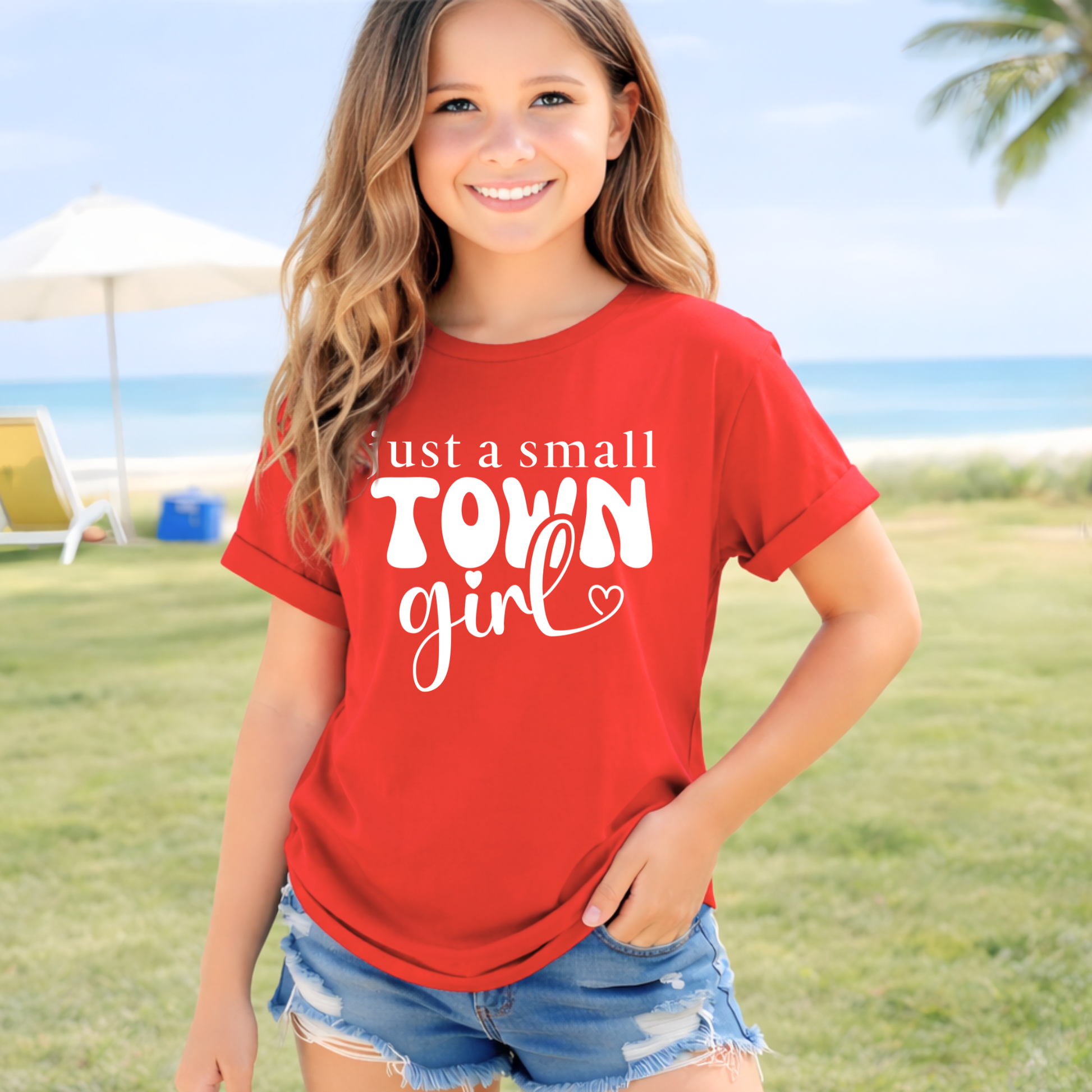 Girl wearing a red t-shirt with 'just a small town girl' text at the beach.