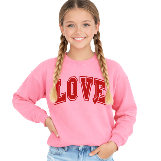 Youth girls pink LOVE sweatshirt with bold red varsity font and heart detail, cozy long sleeve pullover, styled with jeans, front view, cute kids Valentine outfit