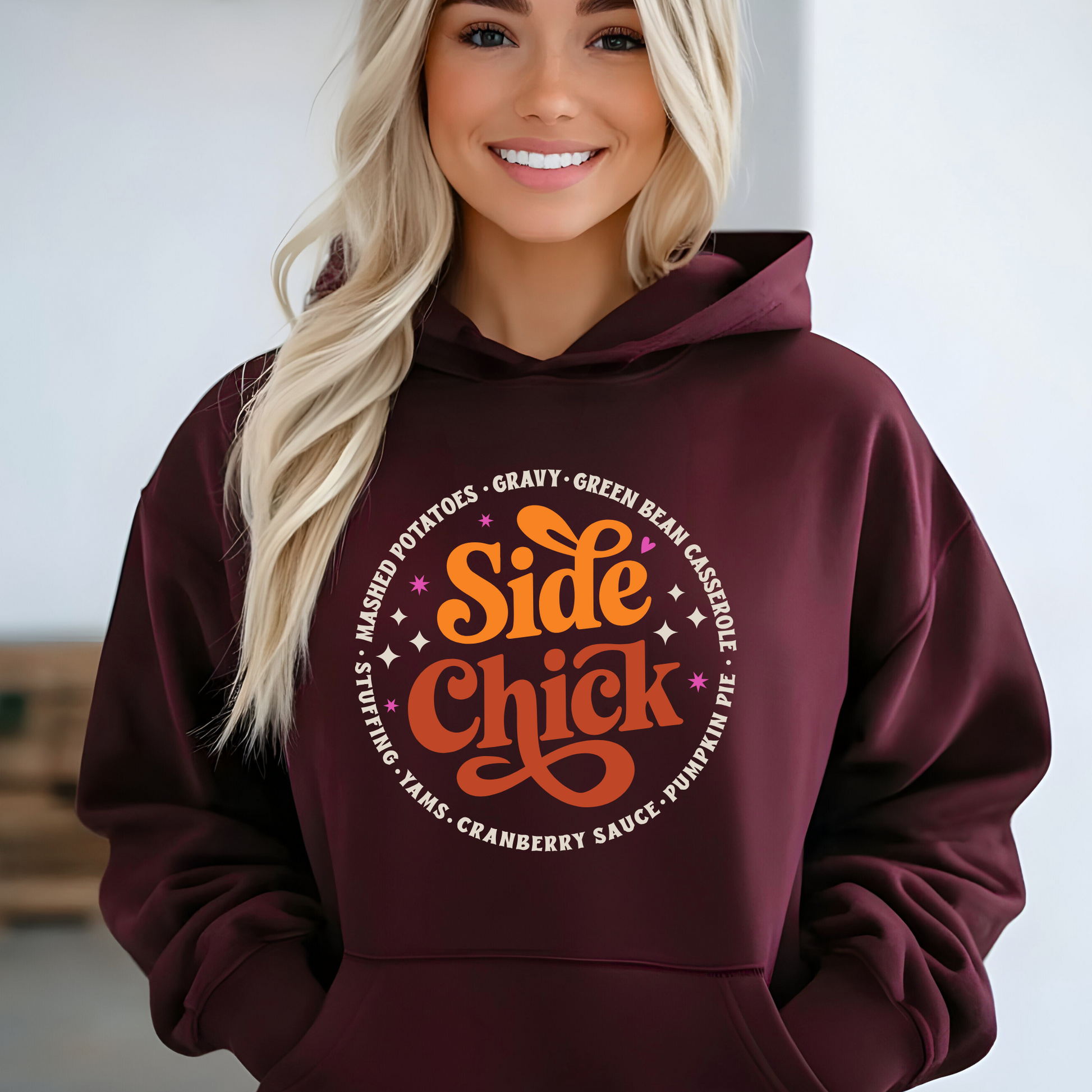 Smiling woman wearing maroon “Side Chick” hoodie with retro fall graphic listing side dishes like stuffing, mashed potatoes, and pumpkin pie. Perfect Thanksgiving pullover for women, great for Friendsgiving and holiday meals.