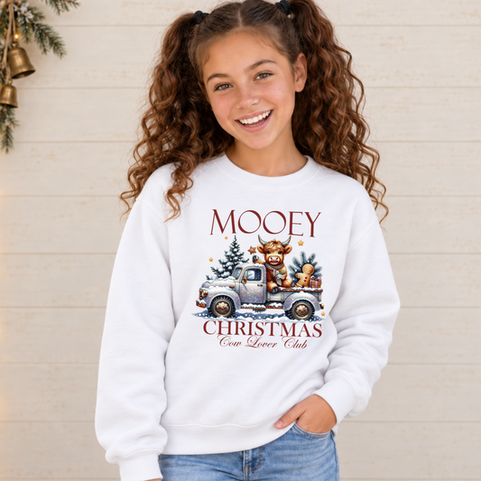 Girl wearing a white Mooey Christmas cow graphic sweatshirt against a light holiday backdrop.