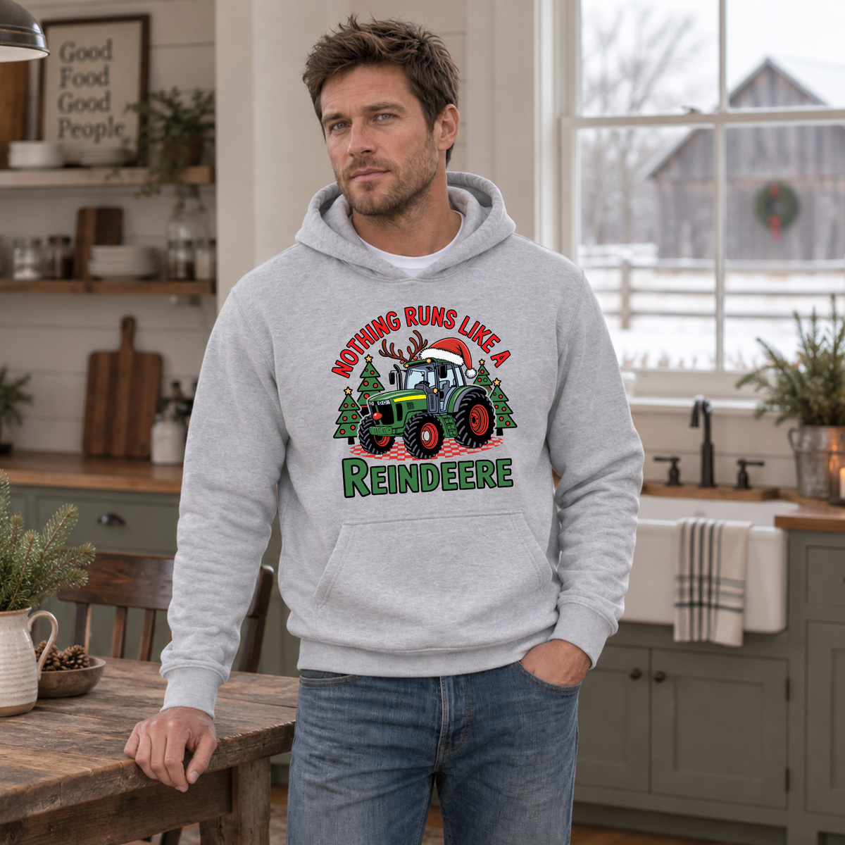 Man in a sports gray Nothing Runs Like a Reindeere hoodie in a farmhouse kitchen with a snowy barn outside.