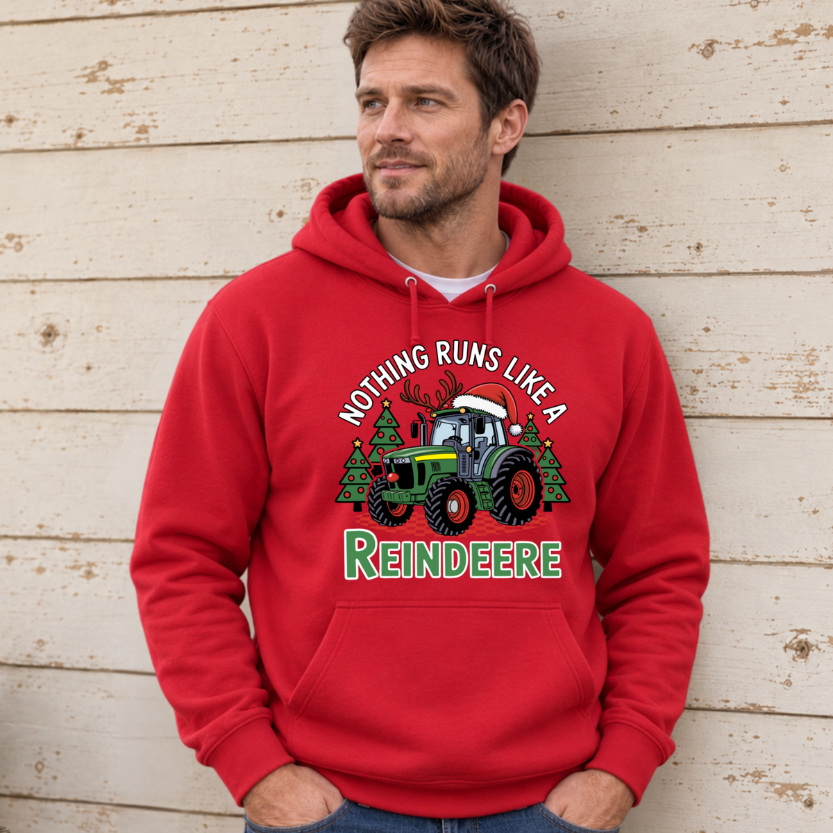 Man wearing a red Nothing Runs Like a Reindeere hoodie against a weathered white wood wall; green tractor with antlers and a Santa hat graphic.