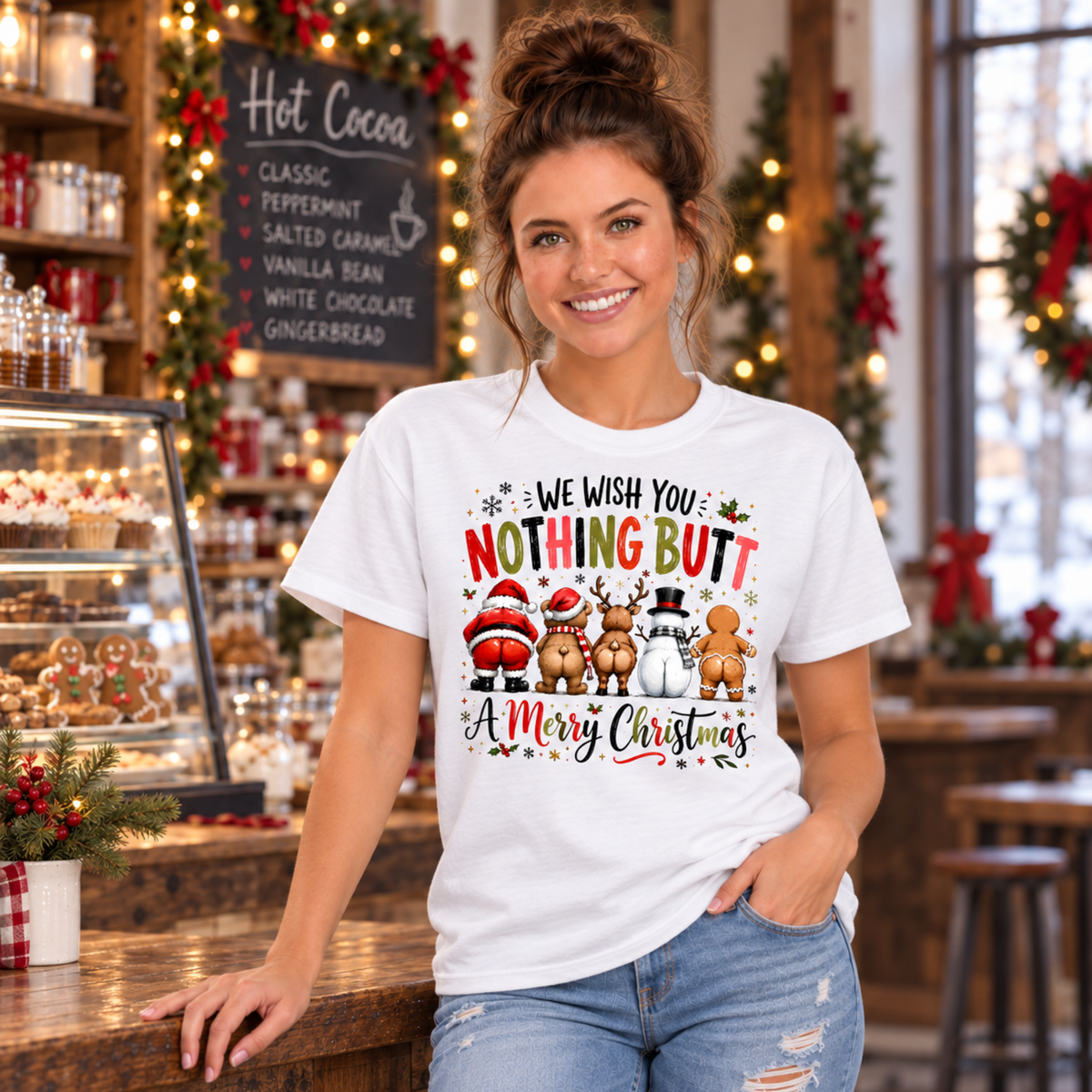 Woman wearing a white T-shirt with We Wish You Nothing Butt a Merry Christmas design with rear-view Santa, bear, reindeer, snowman and gingerbread characters inside a Christmas bakery and cocoa shop