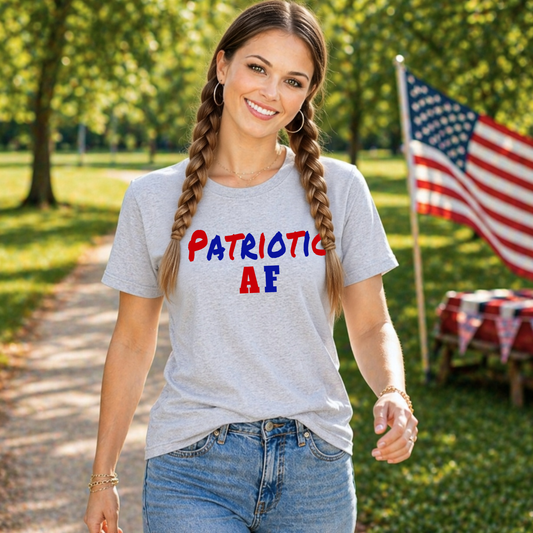 Woman wearing a gray t-shirt with 'Patriotic AF' text, standing outdoors with an American flag in the background.