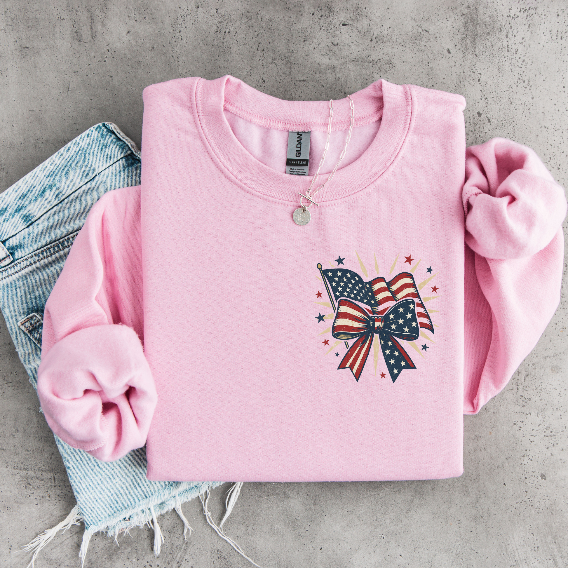 Pink sweatshirt with American flag and bow design on a concrete surface