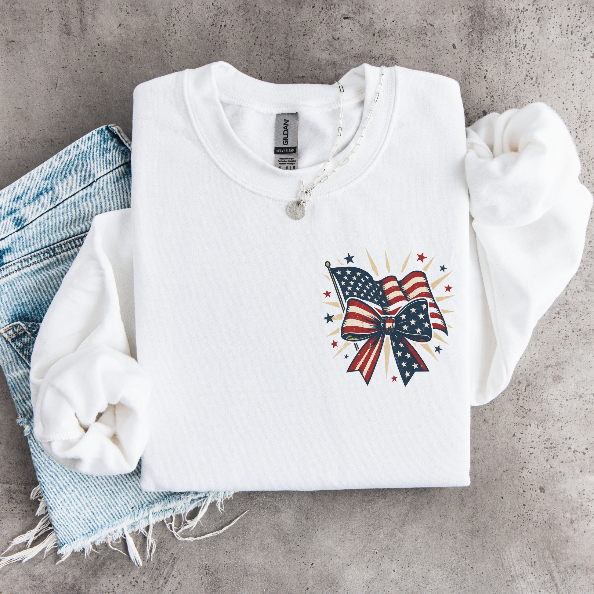 White sweatshirt with American flag bow design on a concrete surface