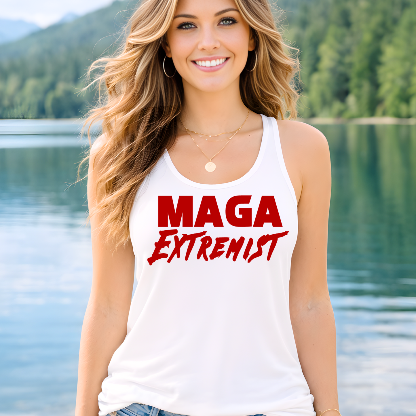 Woman wearing a white tank top with 'MAGA Extremist' text in red, standing by a lake with mountains in the background.