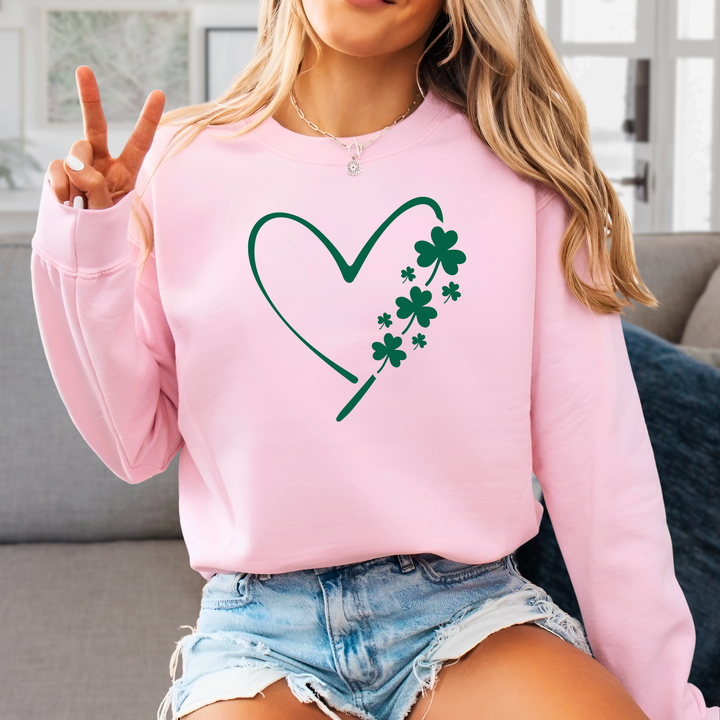 A woman wearing a pink sweatshirt with a minimalist green heart and shamrock design, perfect for St. Patrick’s Day celebrations.