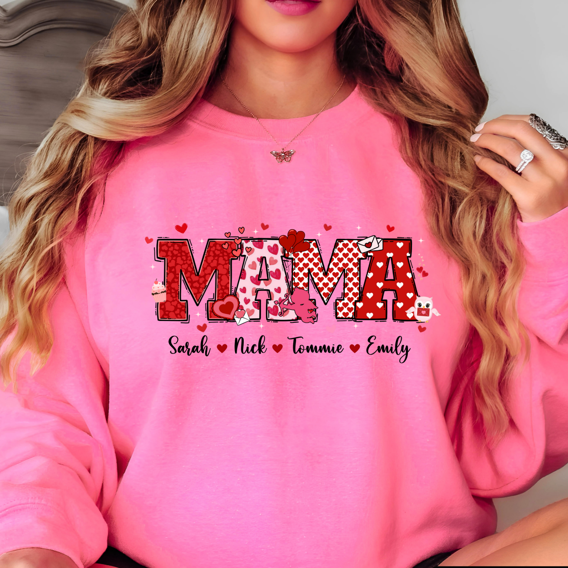 A pink sweatshirt with a personalized Valentine's Day design, including the name 'MAMA' in a decorative font, surrounded by heart shapes and small decorative elements.