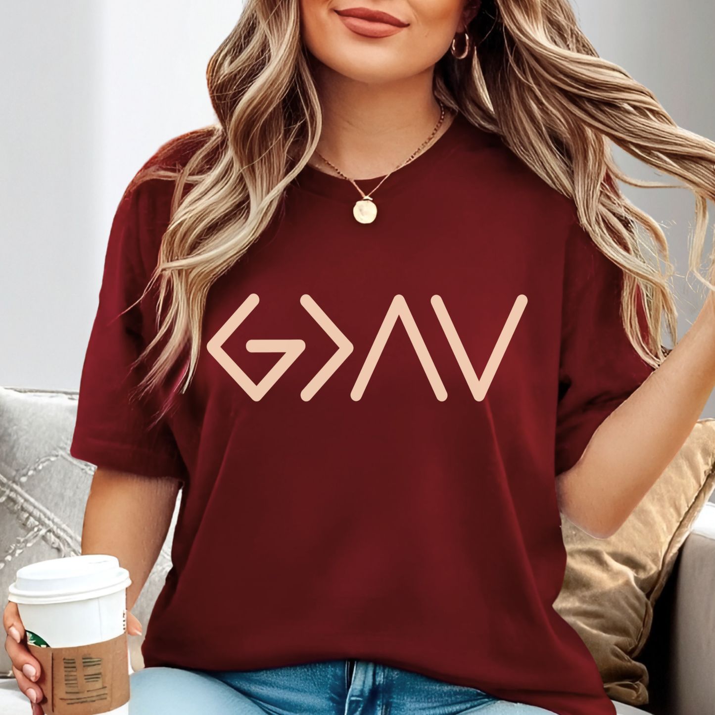 Burgundy short sleeve t-shirt worn by model holding coffee with gold God Is Greater Than the Highs and Lows front design