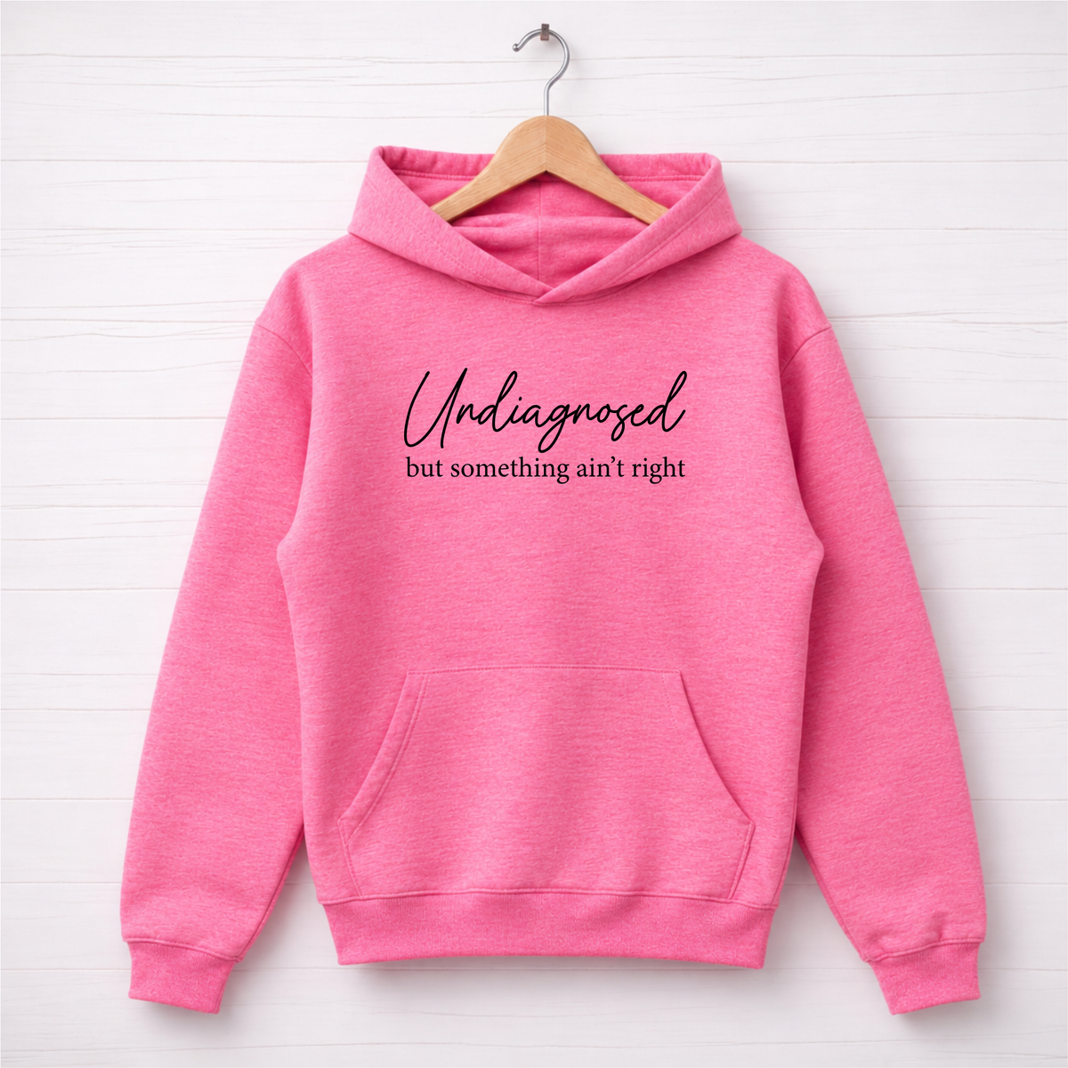 Bright pink hoodie flat lay with black Undiagnosed but something ain’t right graphic text.