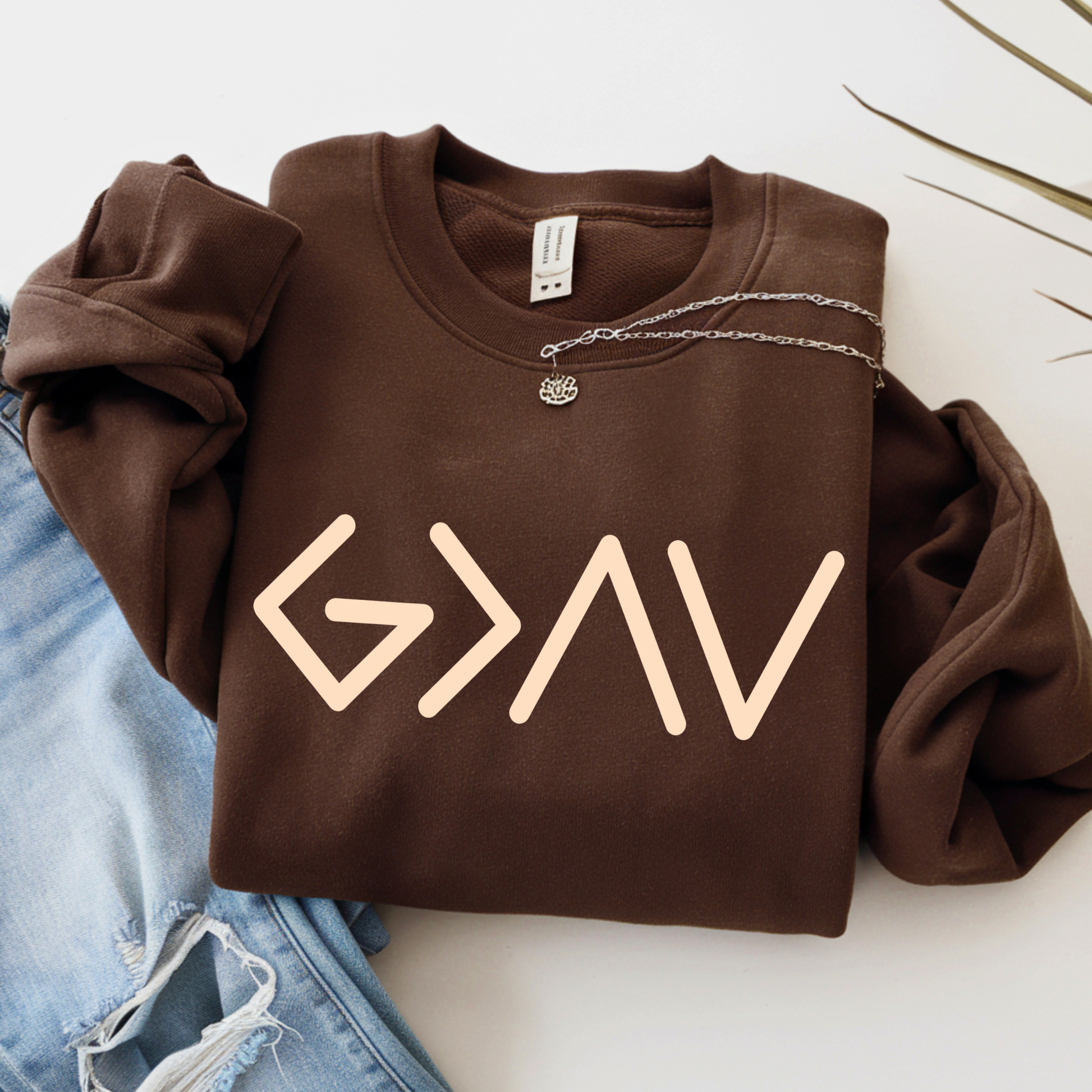 Brown sweatshirt folded displaying gold God Is Greater Than the Highs and Lows front design design