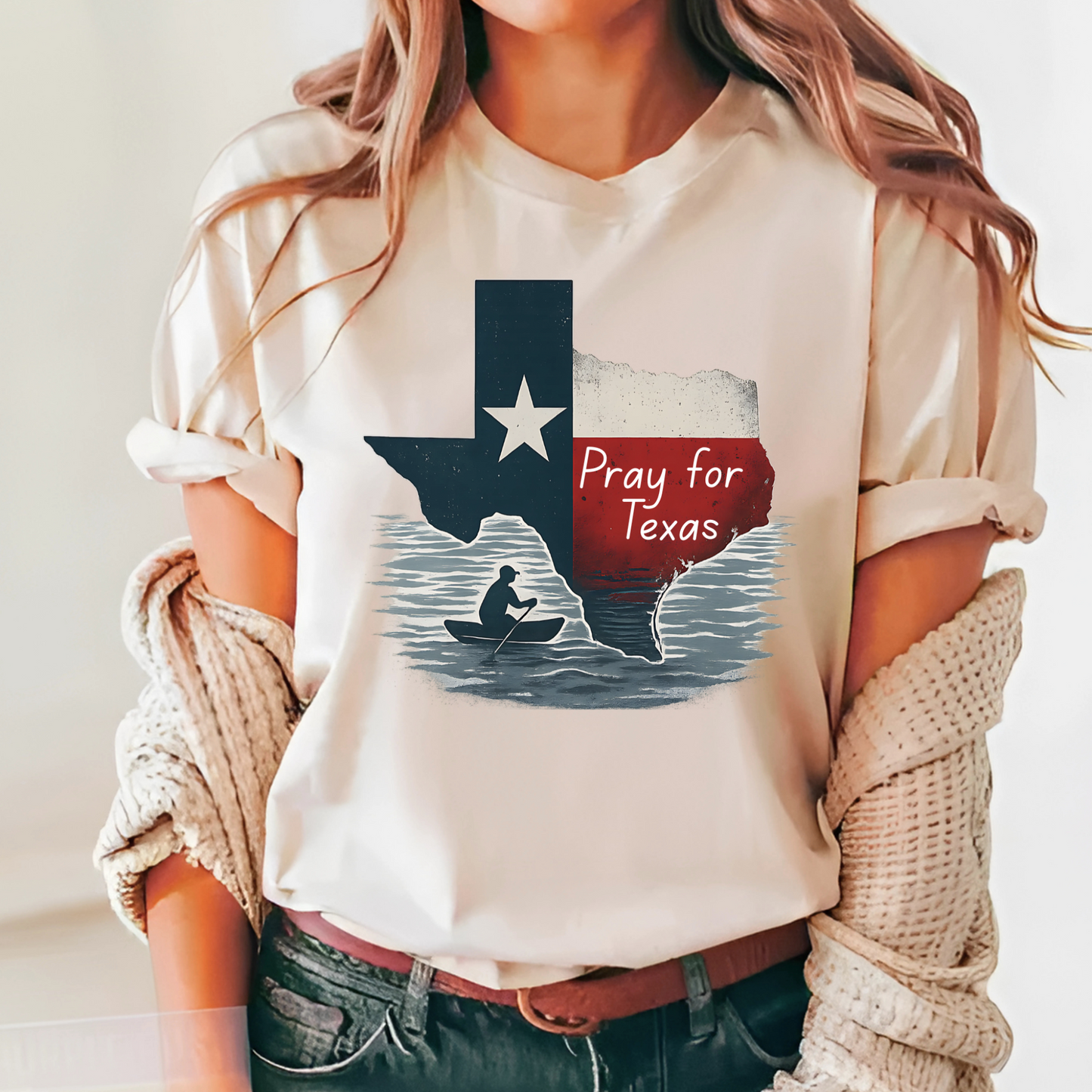 Sand-colored unisex Pray for Texas graphic tee with a rustic Texas flag design and "Pray for Texas" text. Styled with casual denim and layered knit sweater, ideal for showing Texas support in everyday outfits.