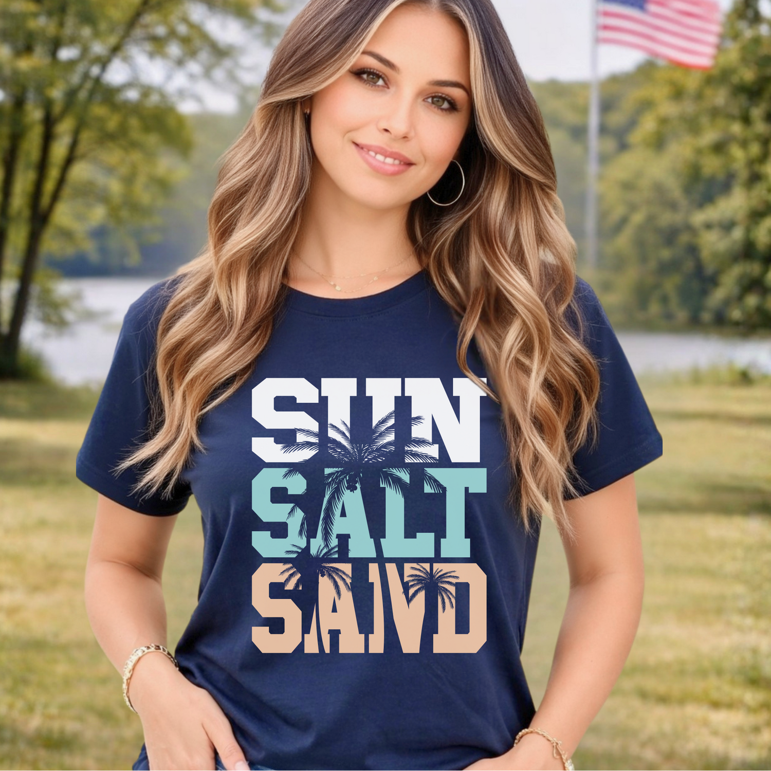 Woman wearing a navy blue t-shirt with 'Sun Salt Sand' text and palm tree graphics outdoors.
