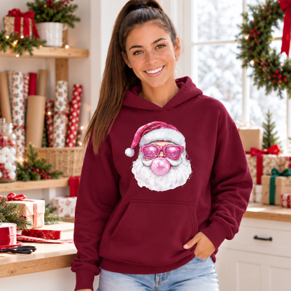 Woman wearing a maroon Bubblegum Santa hoodie beside wrapped gifts in a festive holiday kitchen