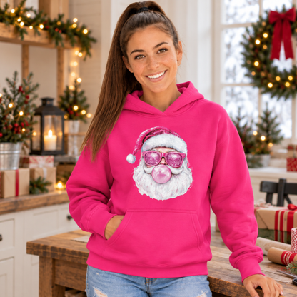 Woman wearing a bright pink Bubblegum Santa hoodie in a festive kitchen with wreaths, lights, and wrapped gifts