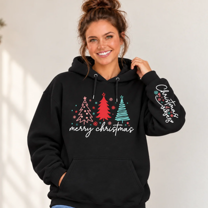 Woman wearing a black hoodie with pink, red, and teal Christmas trees, Merry Christmas front design, and Christmas Vibes sleeve print