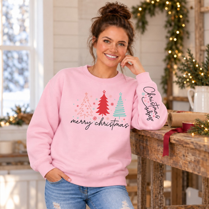 Woman wearing a light pink Merry Christmas tree crewneck sweatshirt with Christmas Vibes sleeve print at a holiday gift-wrapping table