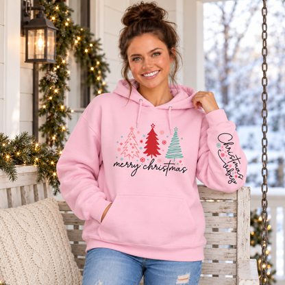 Woman wearing a light pink Merry Christmas tree hoodie with Christmas Vibes sleeve print on a snowy decorated porch