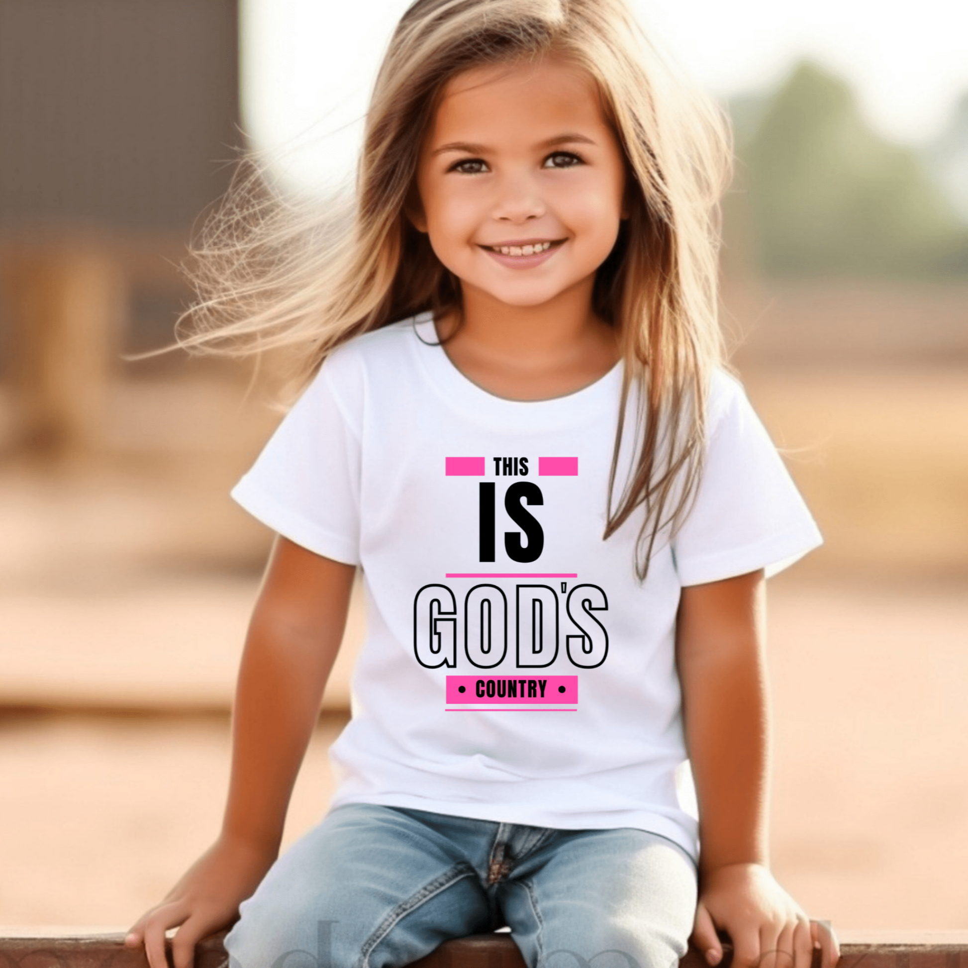 Confident little girl wearing a faith-based 'This Is God's Country' tee, a Christian graphic t-shirt for kids.