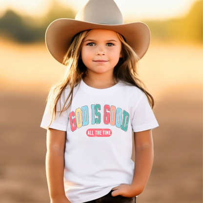 Smiling girl wearing a white T-shirt with the message 'God Is Good All the Time' in colorful text, symbolizing faith and positivity. Perfect for Easter and Christian-themed apparel.