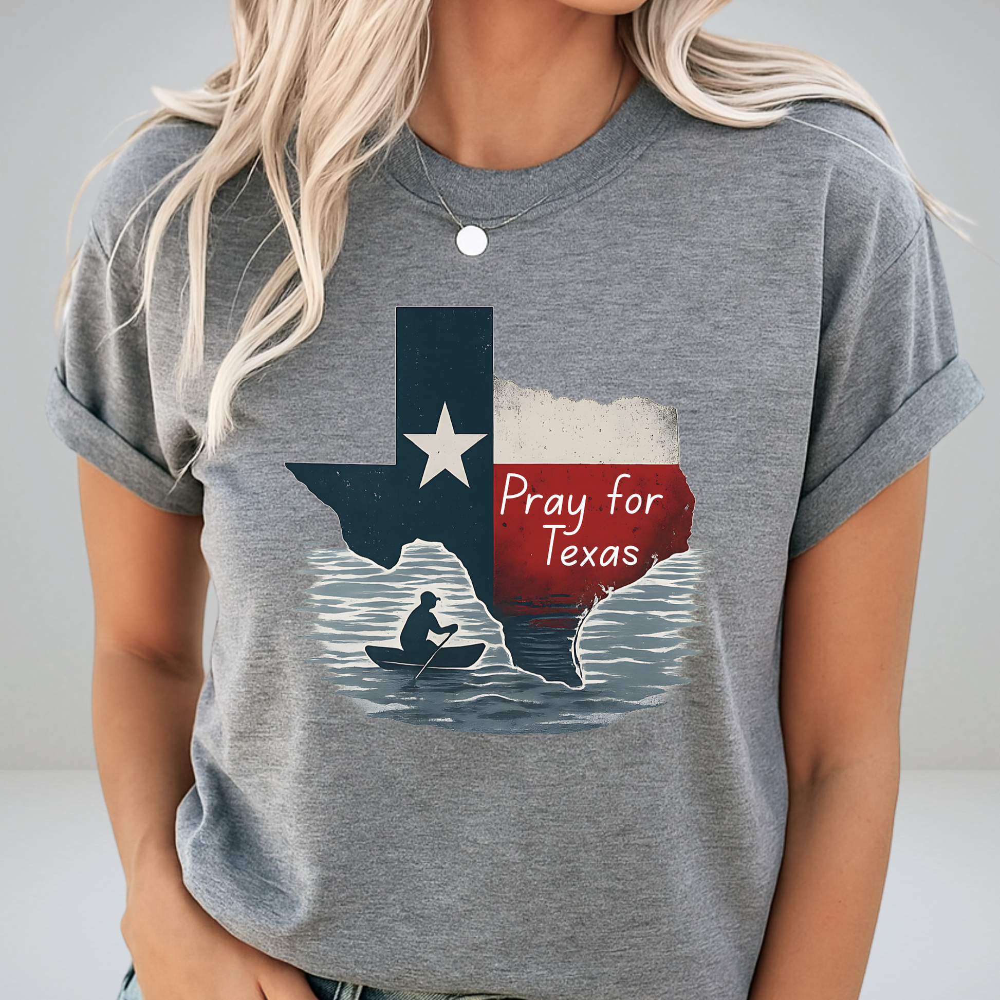 Heather gray unisex Pray for Texas shirt featuring a rustic Texas flag and canoe silhouette. Rolled sleeves and simple accessories create a soft, casual look with Texas support messaging.