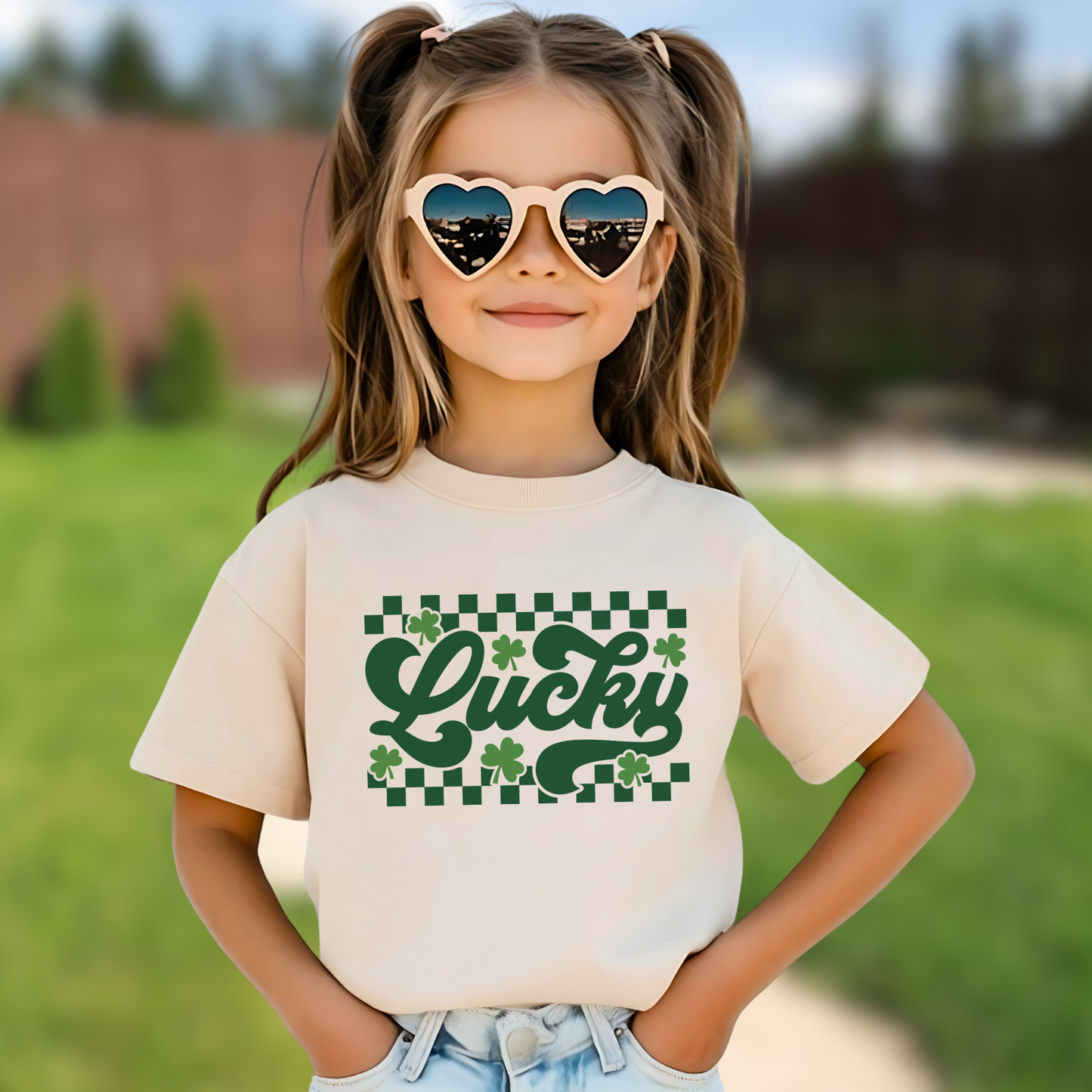 Young girl wearing a sand Festive St. Patrick’s Day T-shirt featuring a green checkered shamrock design for a lucky holiday outfit.